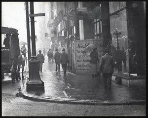 Vandret, sort / hvidt fotografi af fodgængere, der går på Washington Avenue i regnen